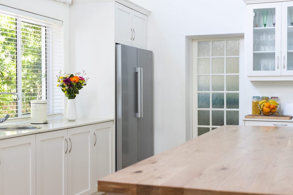 A stainless freestanding refrigerator standing in a cabinetry niche at the end of a kitchen, a wooden worktop running up to it