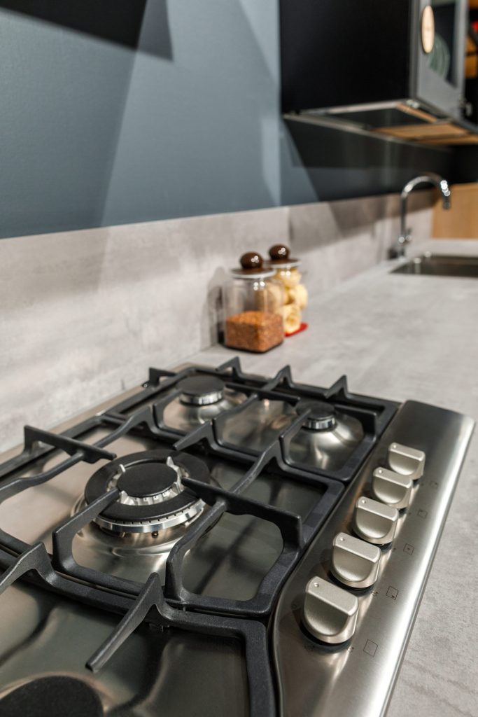 A stainless gas cooktop set into a worktop, cast grates over sealed burners and a row of control knobs along its front edge