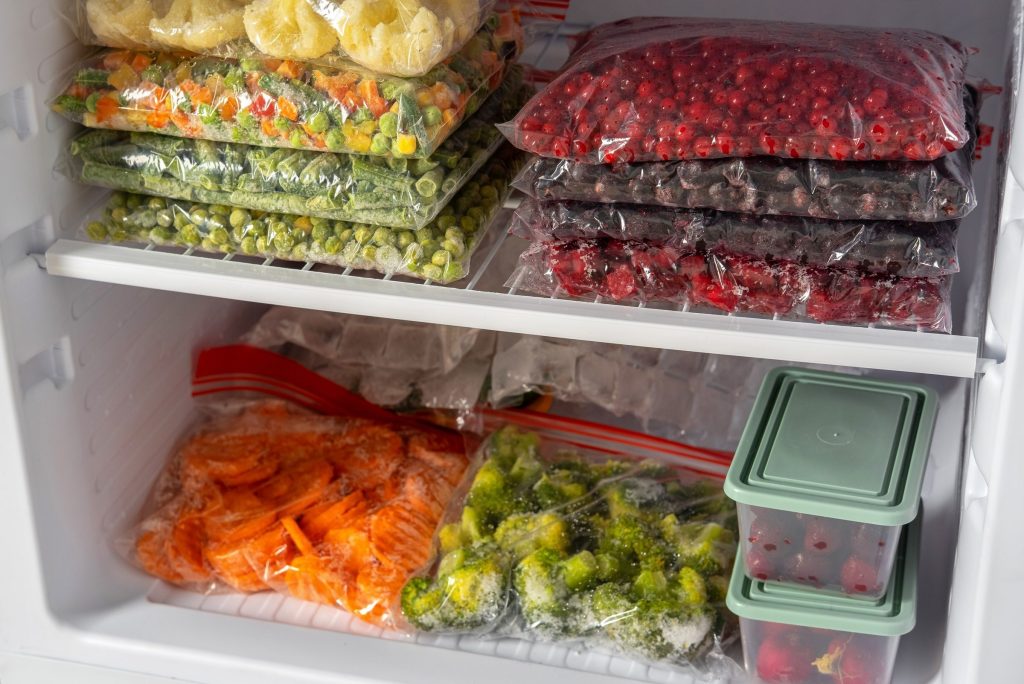 The shelves of a freezer packed with bagged vegetables, berries and containers