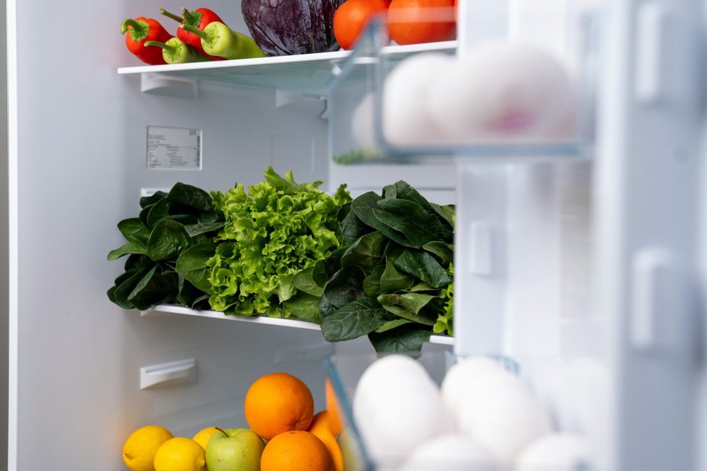 Salad leaves, citrus and eggs on the shelves of an open refrigerator