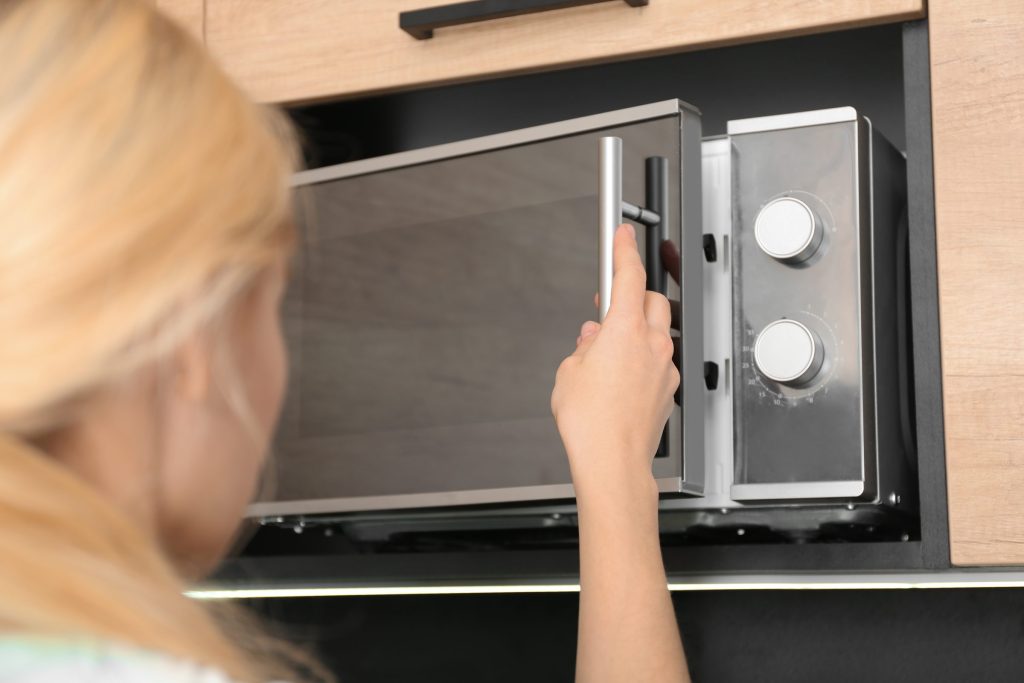 A hand reaching to the controls of a built-in microwave set into a cabinet run