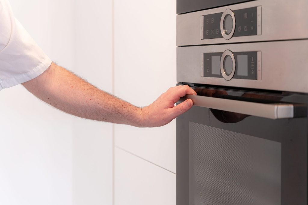 A hand on the handle of a built-in appliance below a microwave in a white column