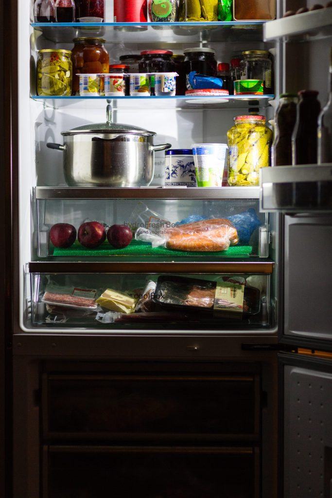 The interior of a built-in bottom-mount refrigerator, shelves loaded with jars and produce and a pan on the top shelf