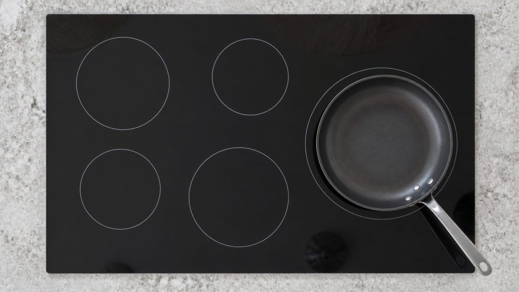 A 36-inch induction cooktop seen straight down, five cooking zones printed as plain rings on the black glass, one pan set on the largest.