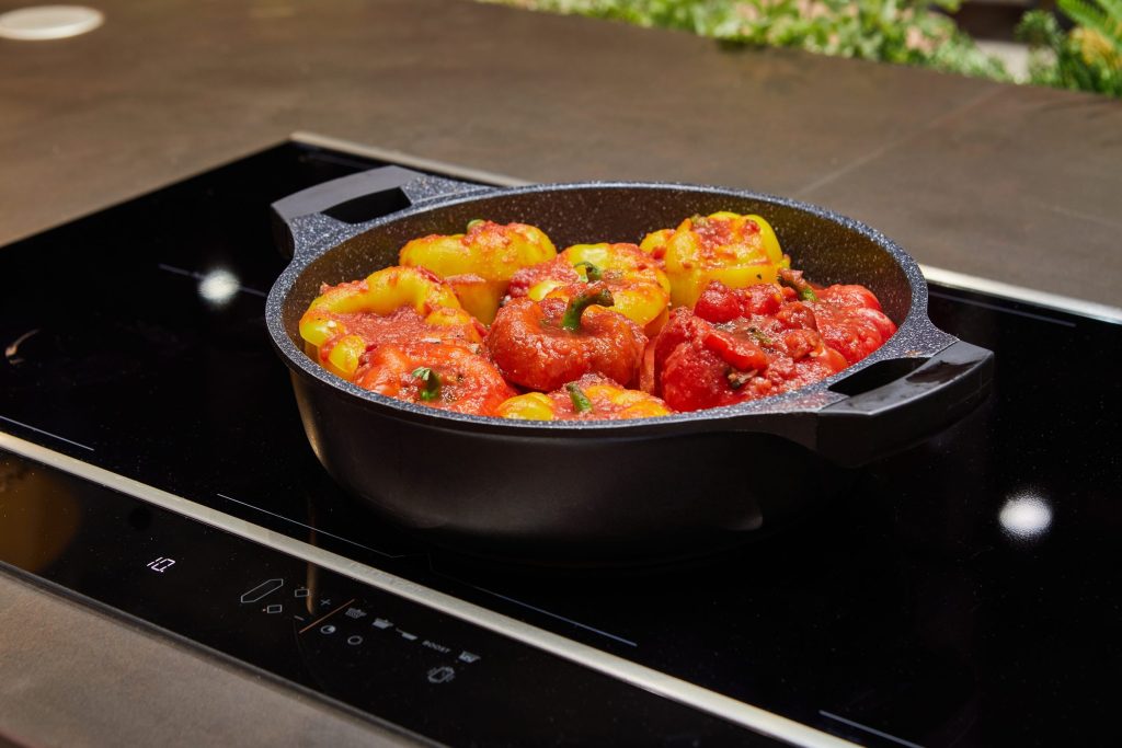 A black induction cooktop with its touch control strip lit, a pan of stuffed peppers on the ring