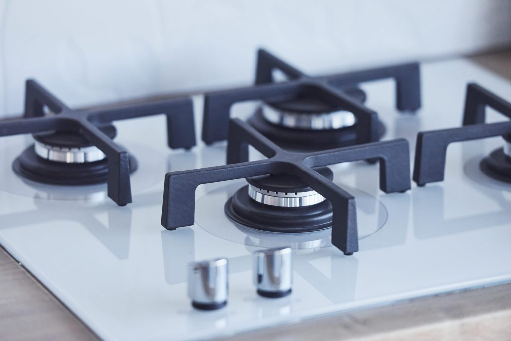 A gas cooktop seen from above, four burners with cast grates on white