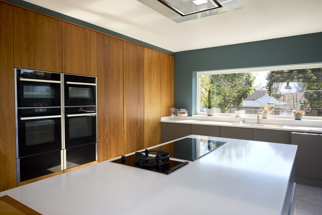 Two stacked built-in ovens set into a walnut cabinet run, with an induction hob on the island in front