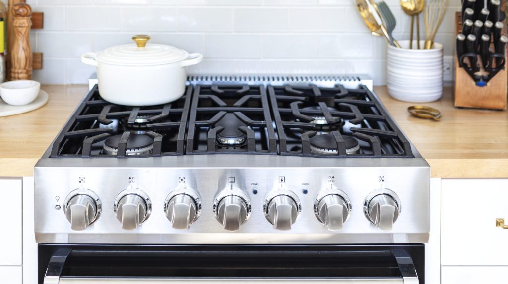 A stainless gas slide-in range with cast-iron grates, seven knobs and a black glass oven door, set into a wood worktop