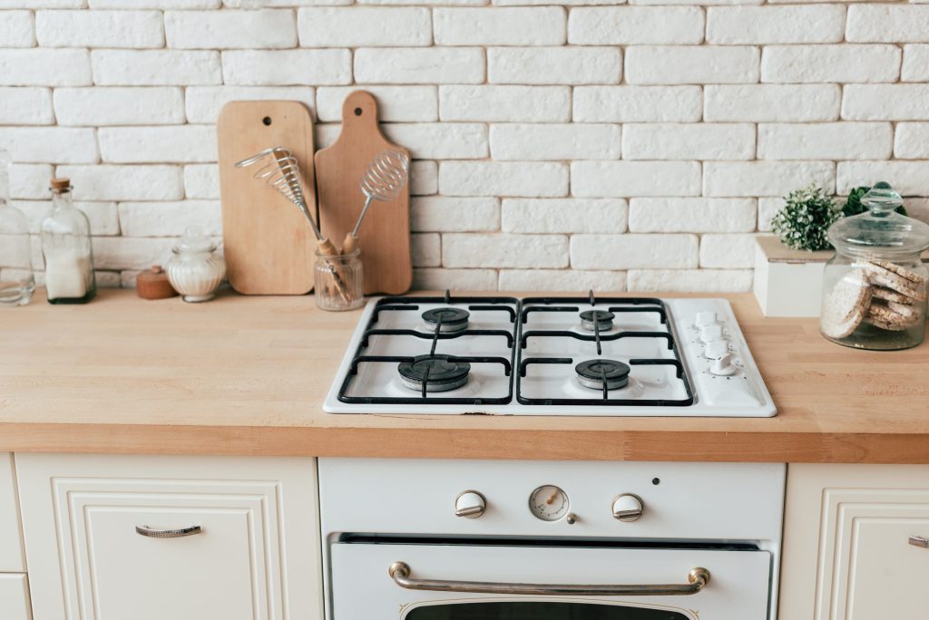 A white gas range in a bright kitchen, four burners on a wooden counter with the oven below