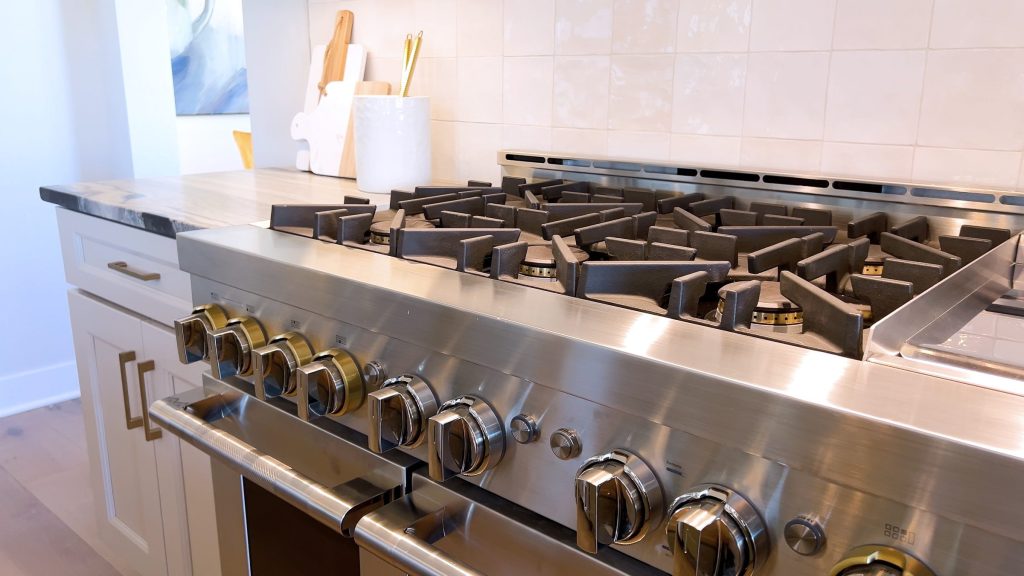 A wide professional gas range in a home kitchen, cast-iron grates and a row of metal control knobs