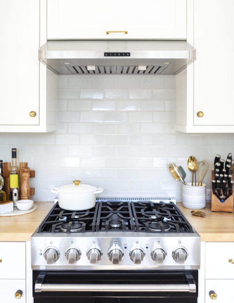 A stainless professional-style gas range with heavy cast-iron grates, set between white cabinets under a hood