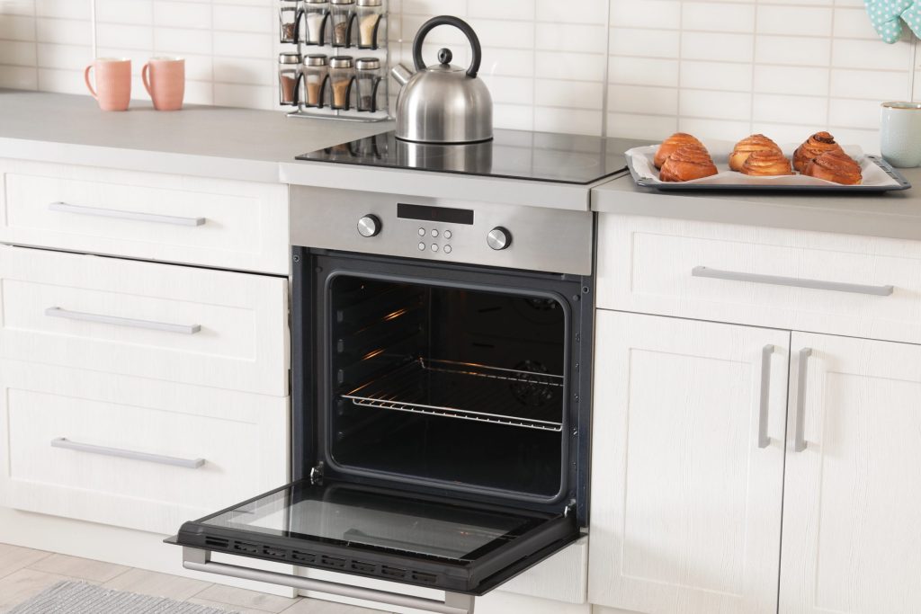 A stainless oven open with a tray cooling above it