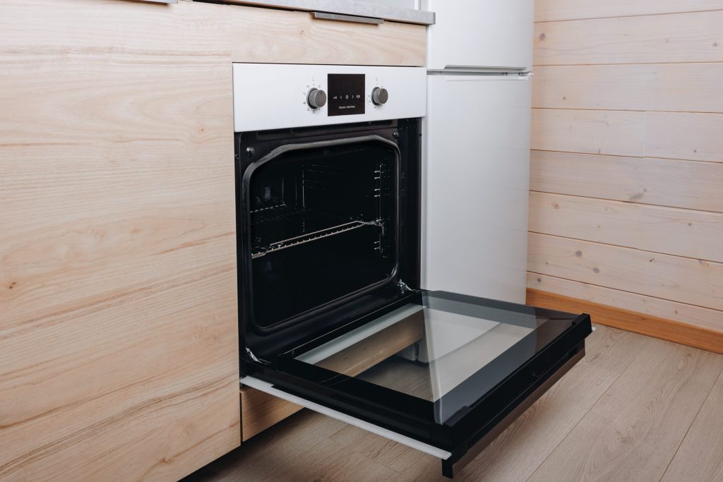 A white built-in oven open against a pale timber wall
