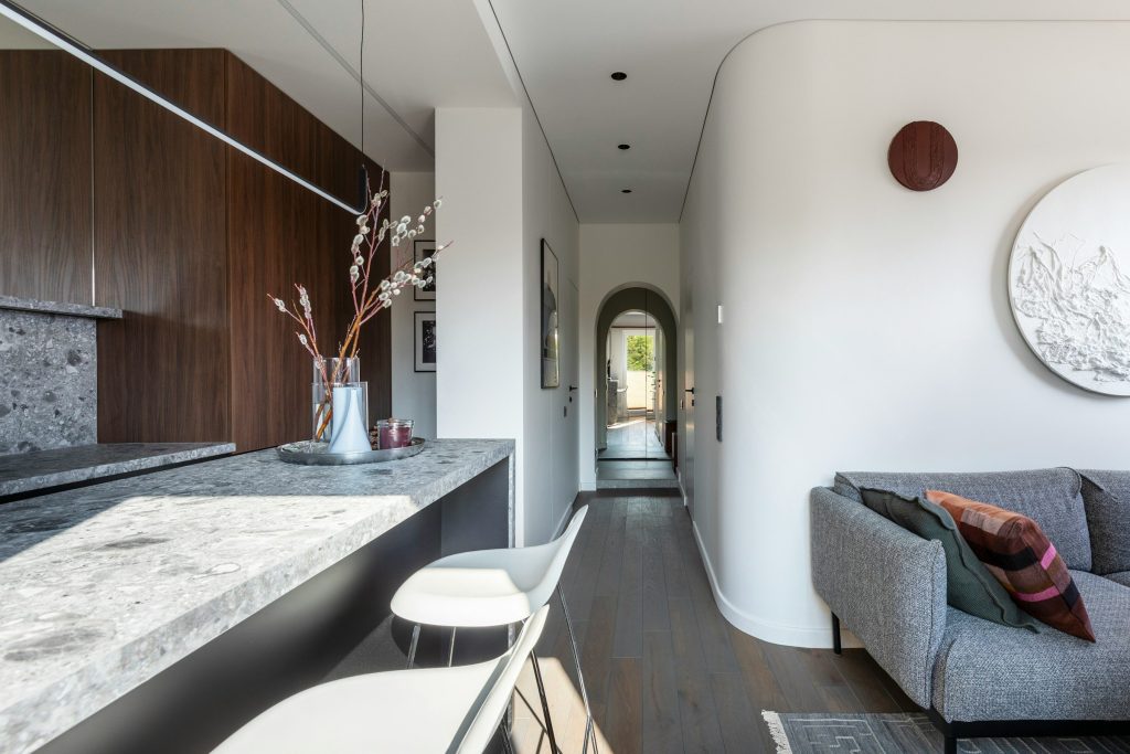 A long stone counter running down a hallway kitchen, stools at the far end and a sitting area beyond
