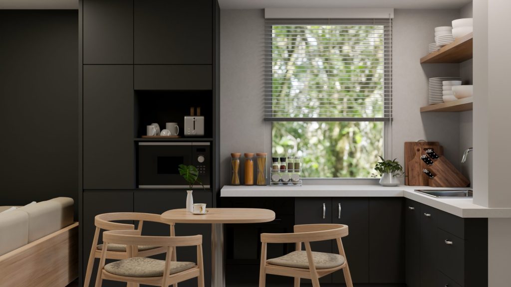 A dark kitchen run beside a window with a small round table and light chairs in front of it