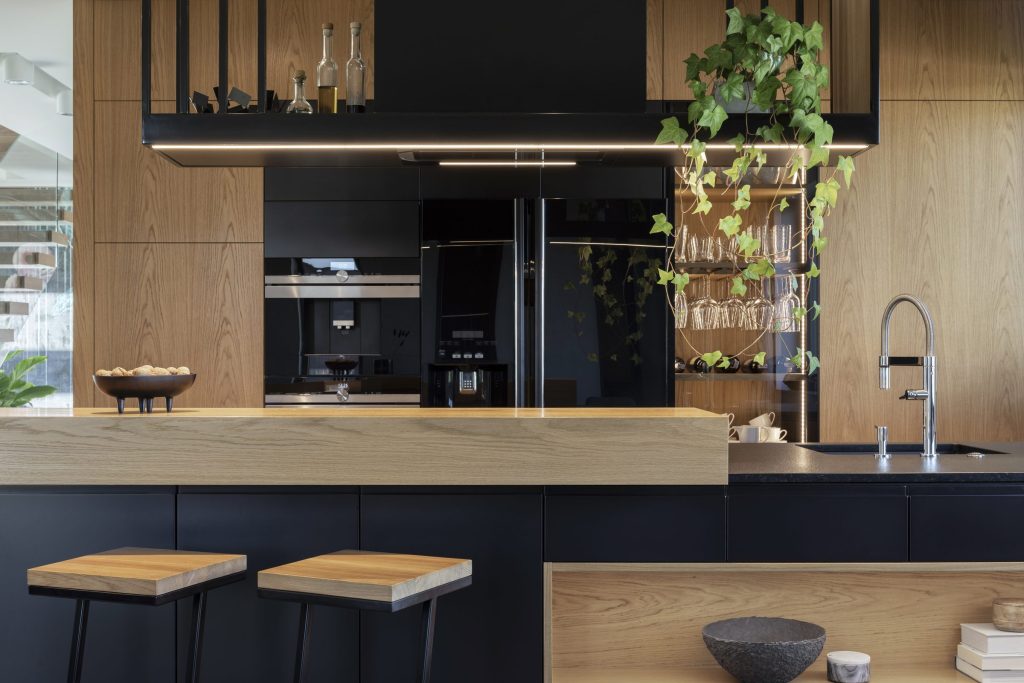 A wall of built-in appliances in a dark kitchen — oven, coffee system and a tall refrigerator beside oak cabinetry