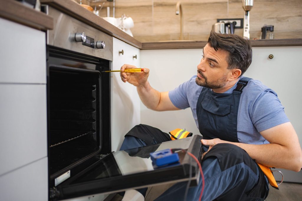 A technician taking a reading at the open door of a built-in oven, meter in hand