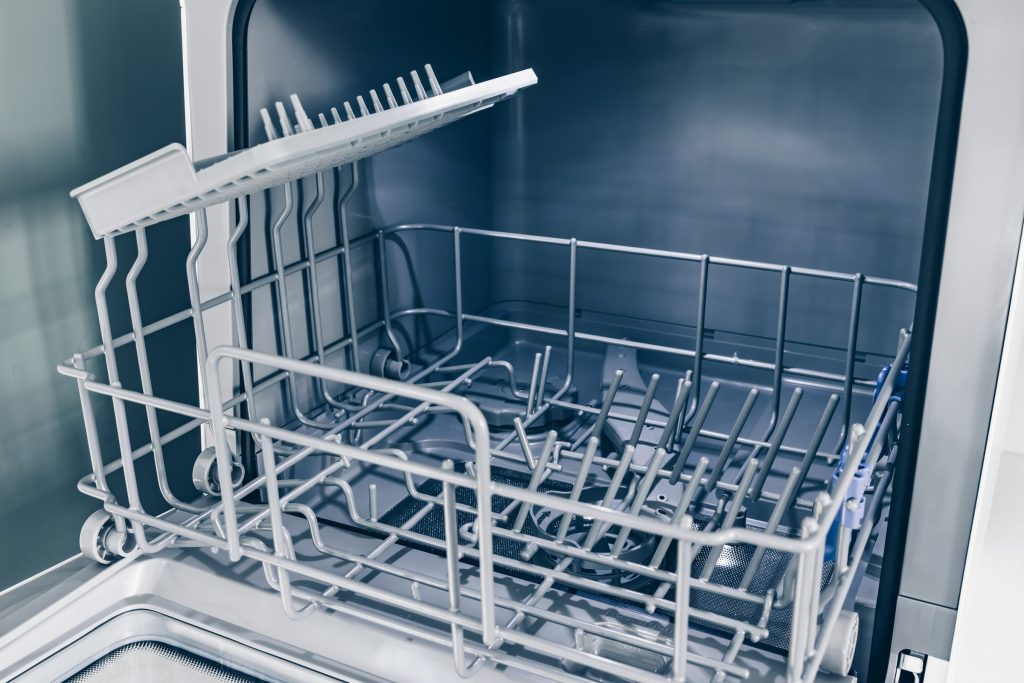 The empty racks and tub floor of a dishwasher standing open