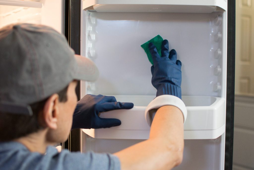 A technician in gloves working along the door shelf and seal of an open refrigerator