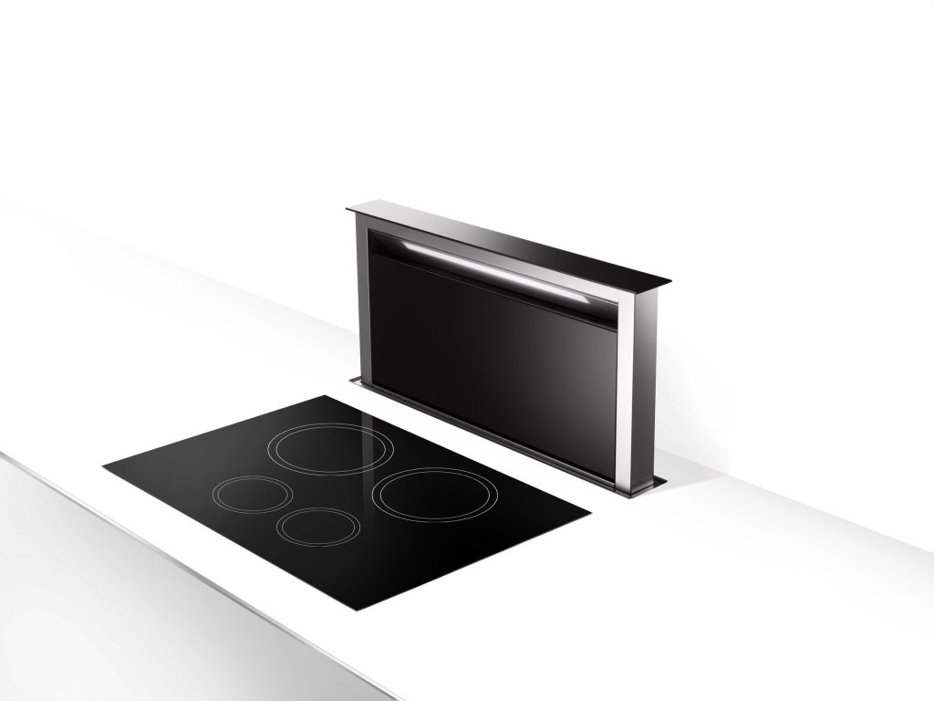A downdraft vent raised out of the counter behind a black glass cooktop