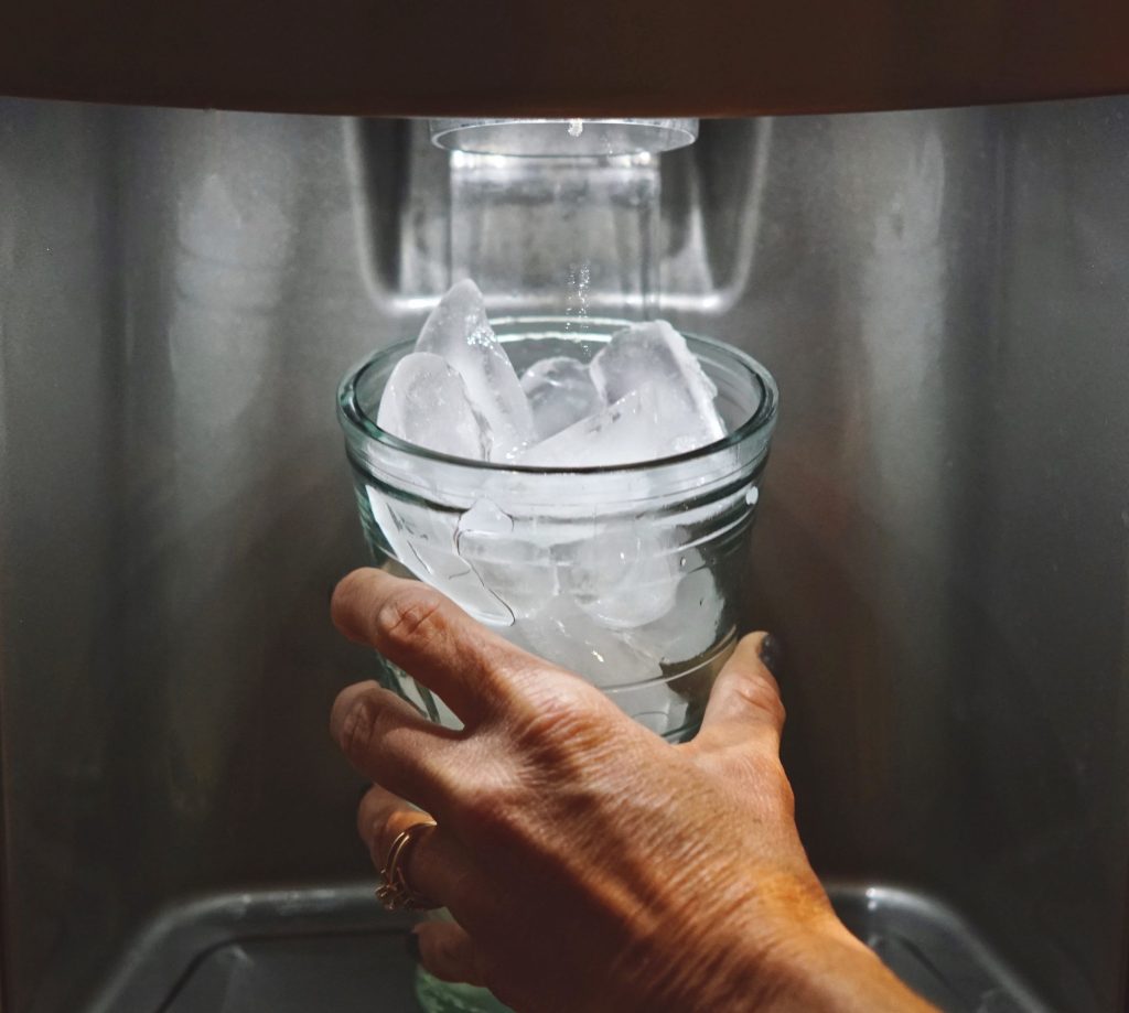 A hand holding a glass under a dispenser as it fills with ice