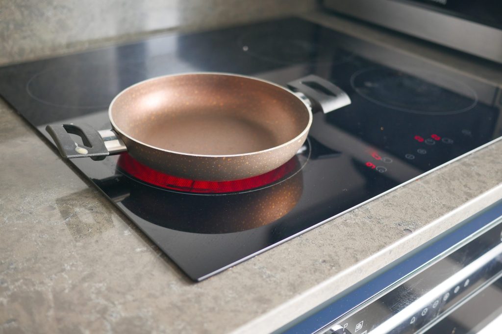 A copper pan on a black induction cooktop set into a stone worktop