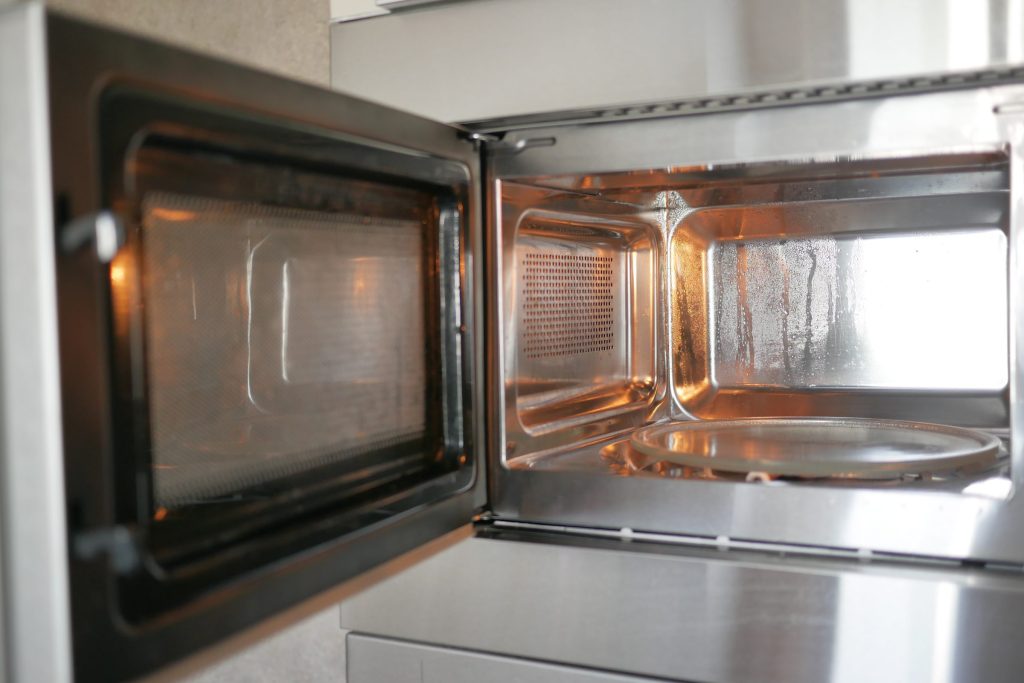 The open cavity and door of a built-in microwave, turntable and interior lit