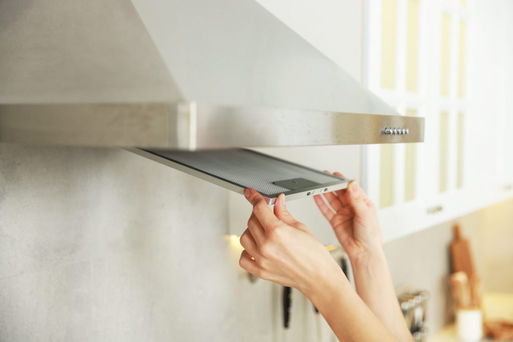 Two hands lowering the filter panel out of the underside of a kitchen extractor