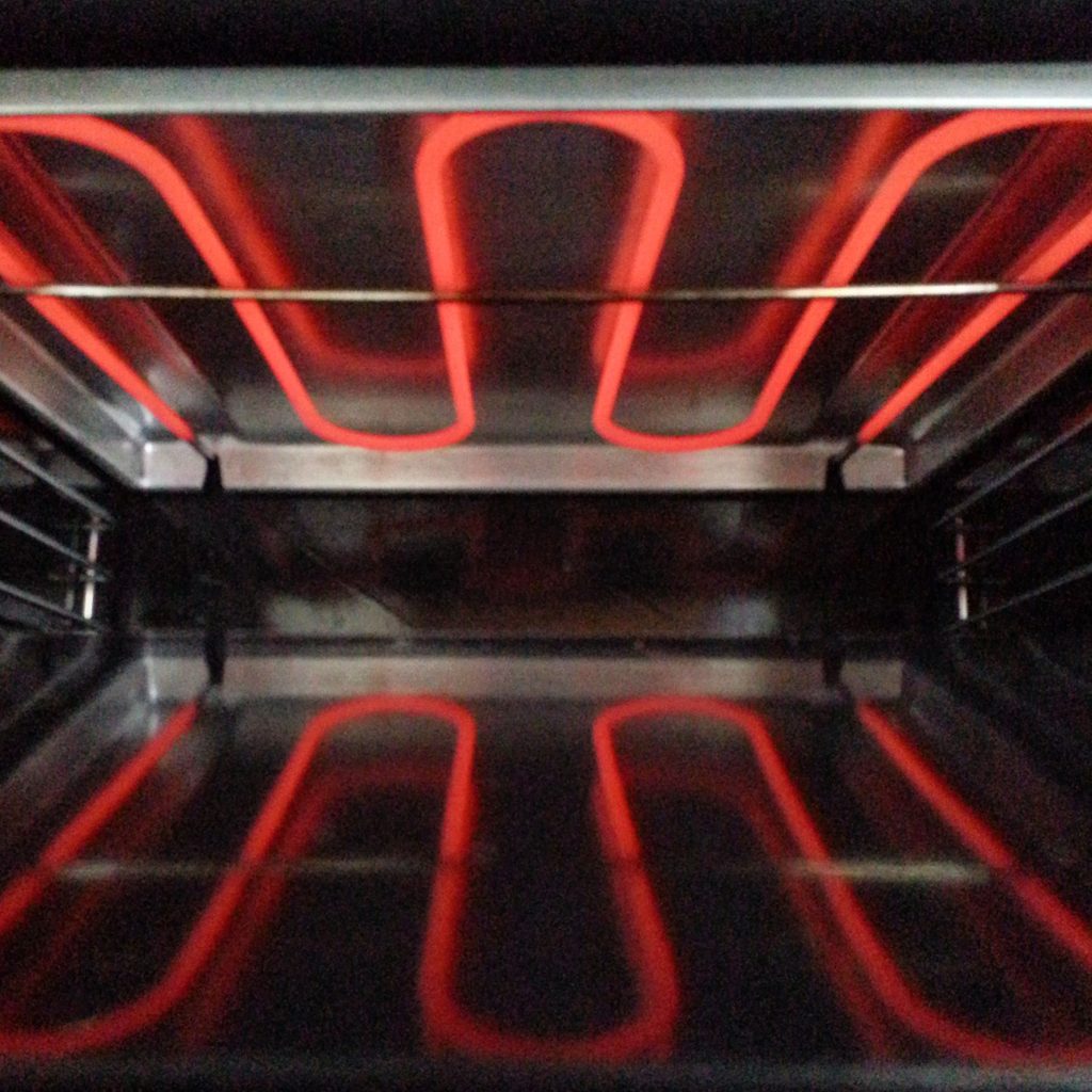 The elements of an oven glowing red across the top of a dark cavity