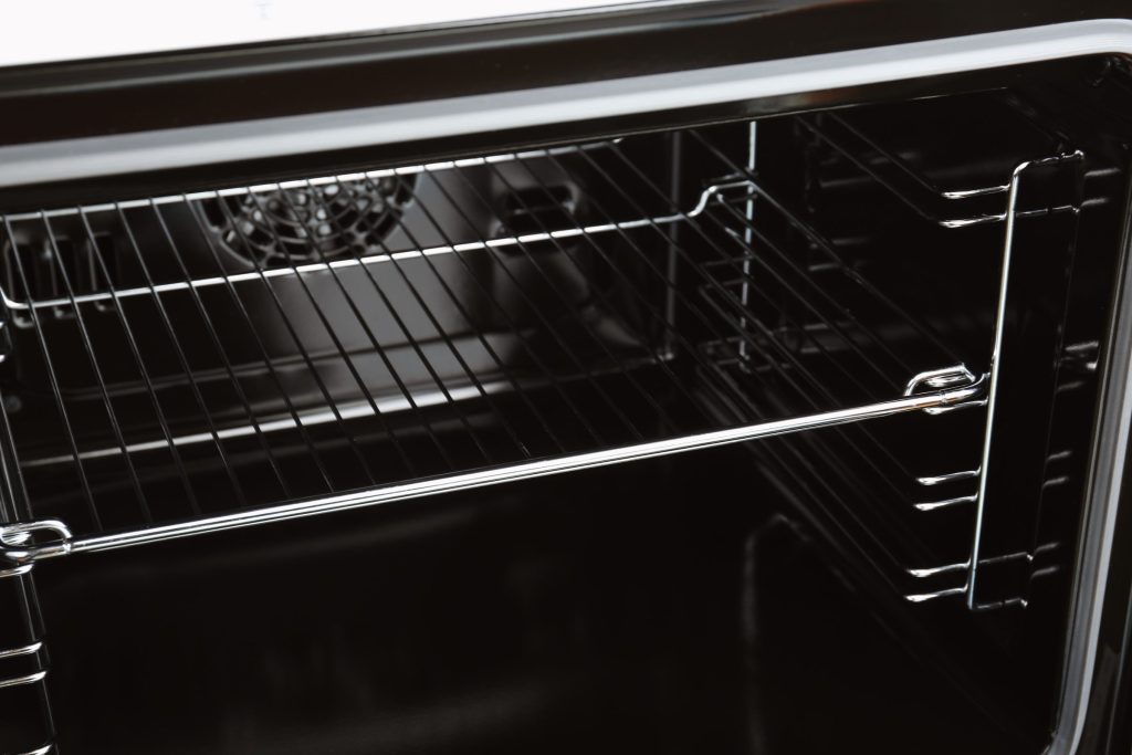 The empty cavity of a wall oven with its wire racks in place, the fan cover on the back wall