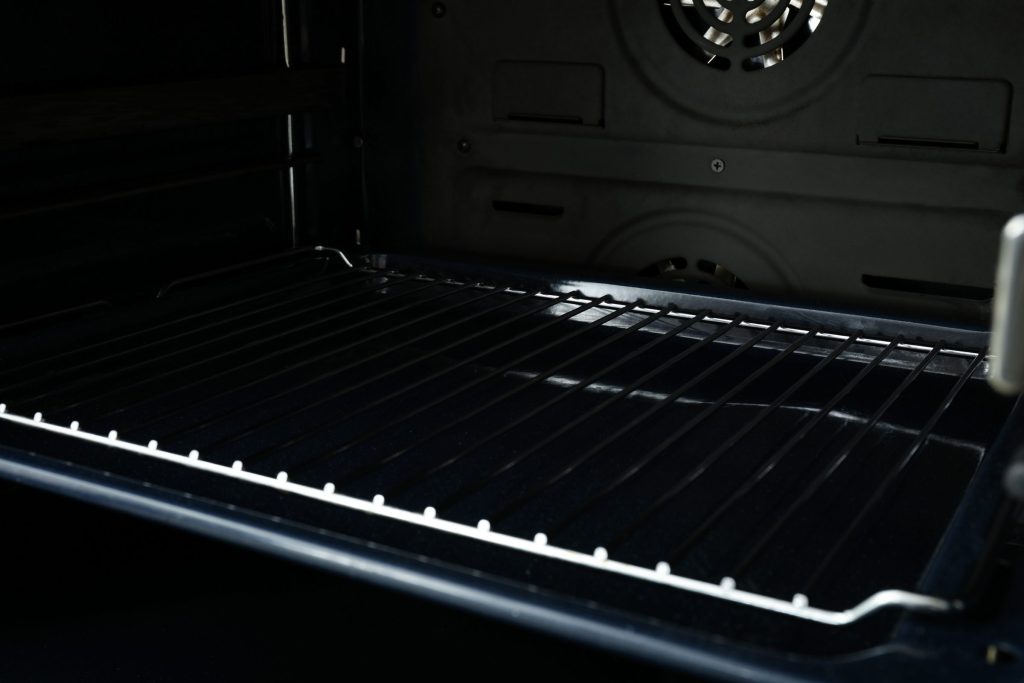 The dark interior of an oven cavity, unlit, racks and rear fan cover just visible