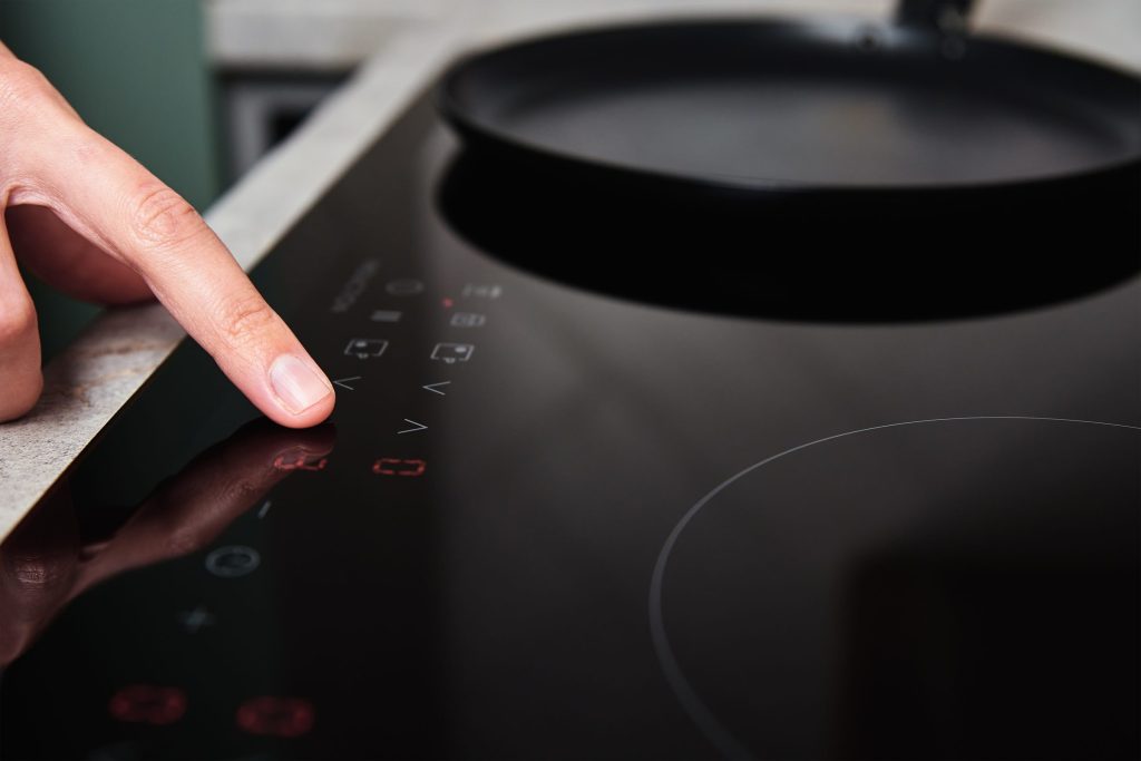 A finger resting on the touch control strip of a dark induction cooktop