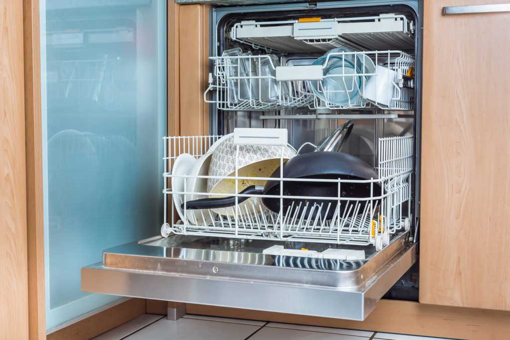 A built-in dishwasher standing open with both baskets loaded