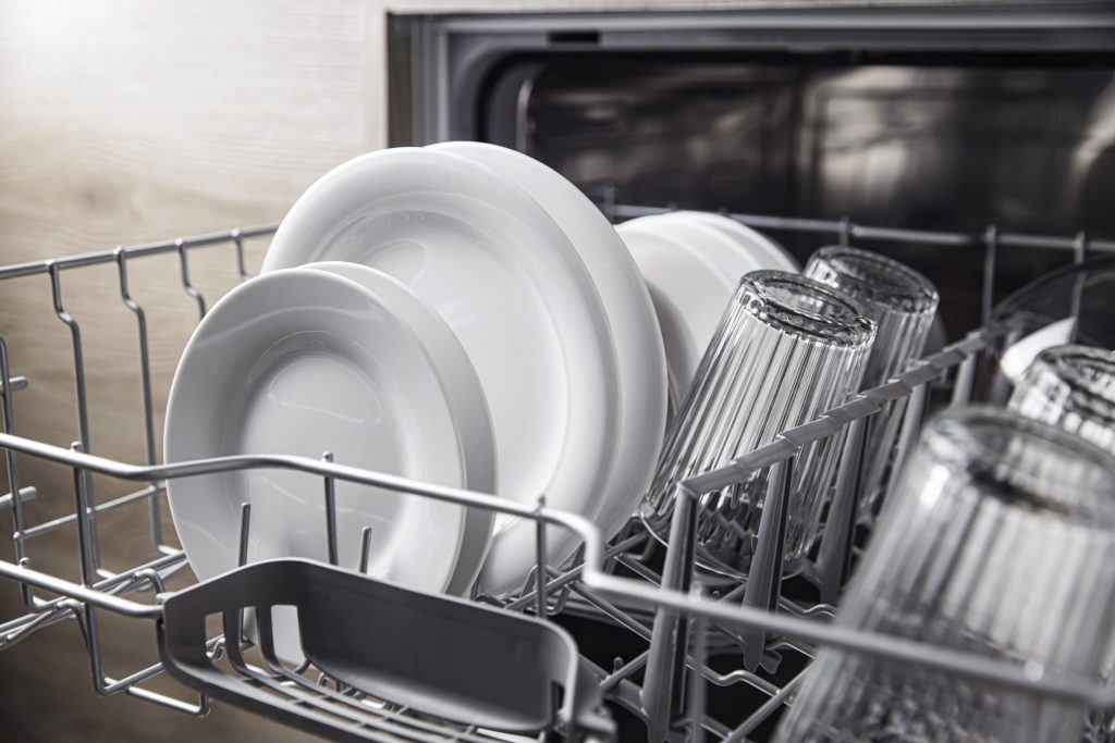 Plates and glasses standing in the upper basket of an open dishwasher