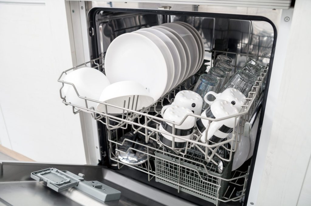 Plates and cups stacked in the baskets of an open dishwasher