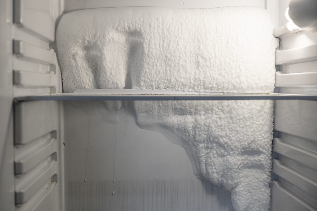 A thick slab of frost across the back wall and shelf of a freezer compartment