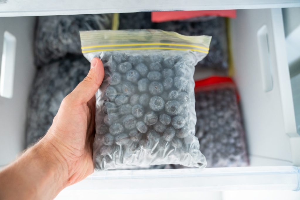 A hand lifting a bag of frozen berries out of a freezer drawer