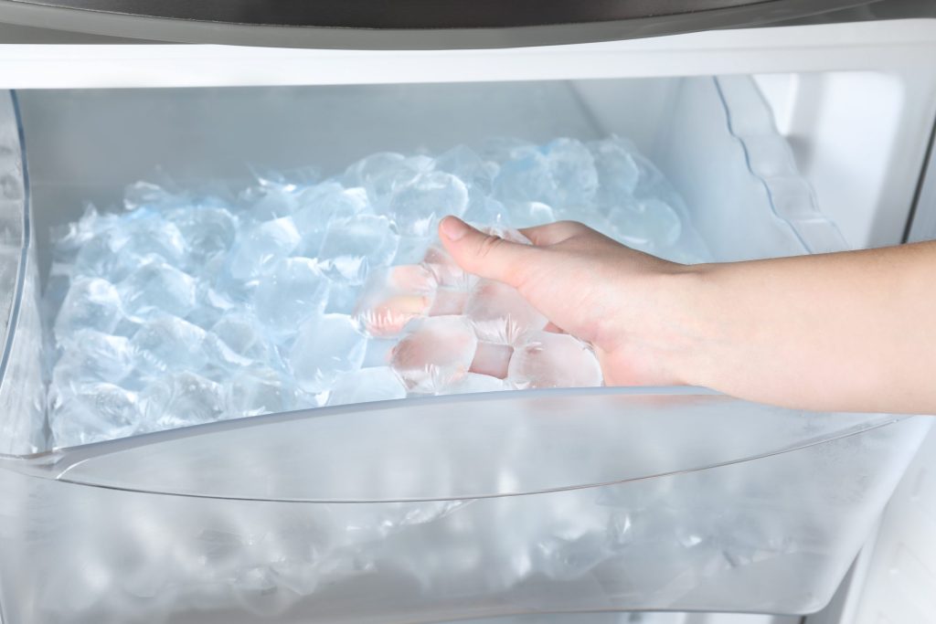 Two hands in the ice bin of a machine, cubes heaped to the front