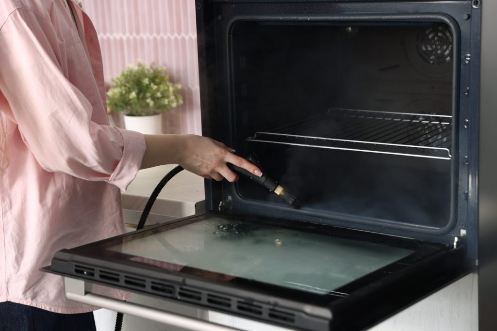 A person wiping down the inside of an oven door with the door lowered