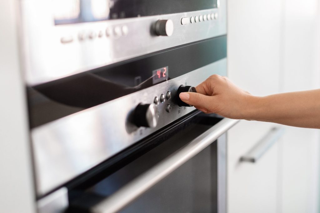 A hand turning the control dial on the fascia of a built-in oven
