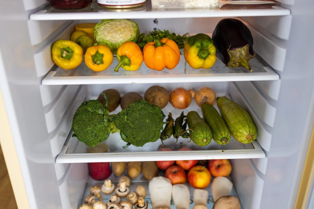 Peppers, broccoli and vegetables arranged on the shelves of an open refrigerator