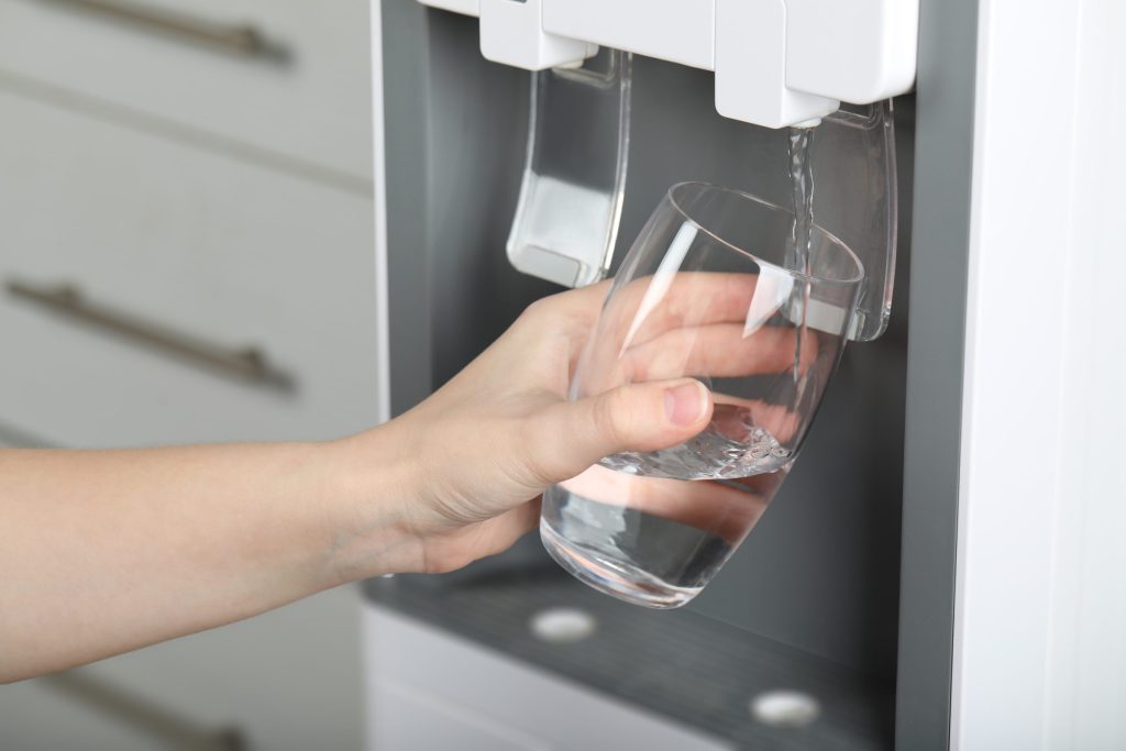 A hand holding a glass under the water dispenser in a refrigerator door