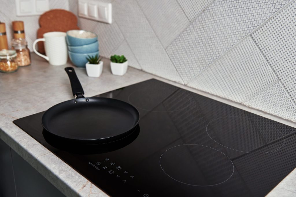 A frying pan on a black induction cooktop, its touch control strip unlit along the front edge