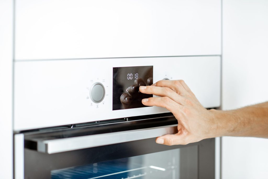 A hand reaching to the control panel of a built-in oven set into white cabinetry