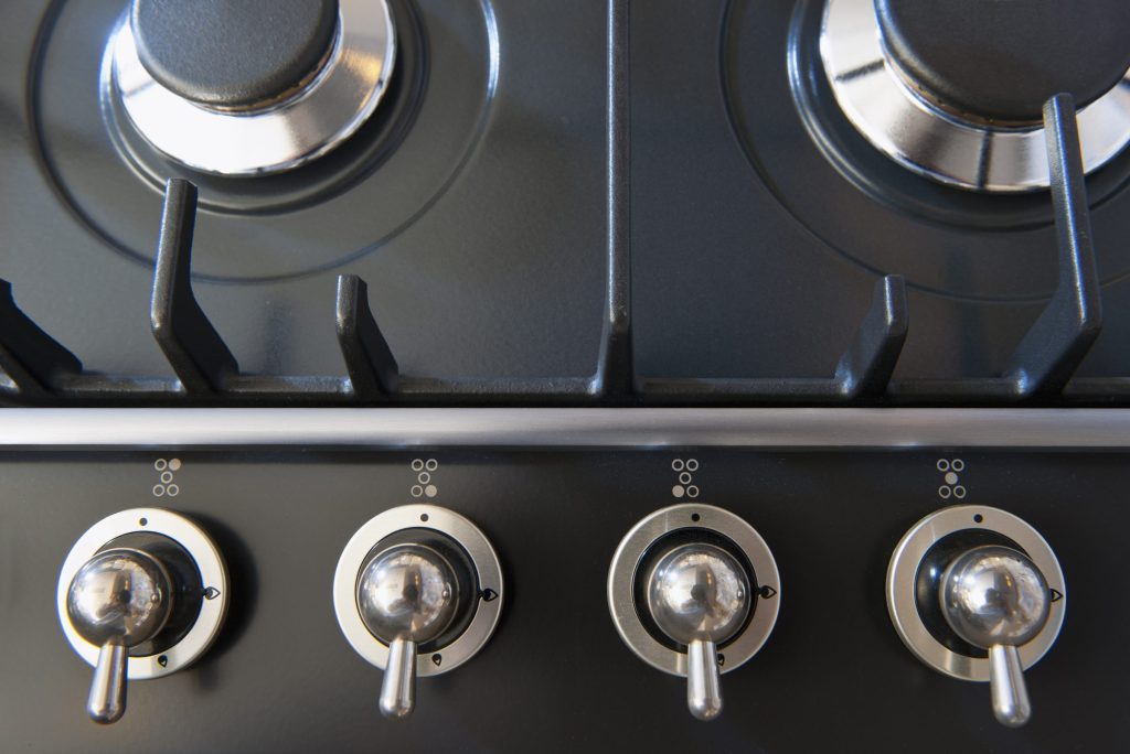 Four lever knobs in a row below the burners of a dark range