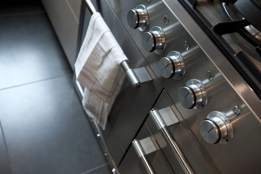 A towel hanging from the handle of a stainless range, its knobs in a row alongside